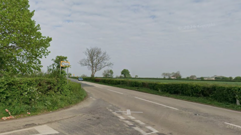 A road junction, showing the A39. It is a rural road, surrounded by green fields and trees. 