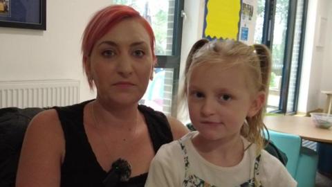 Mia sitting on the lap of her mother, Sian, who has pink hair. They are both looking at the camera