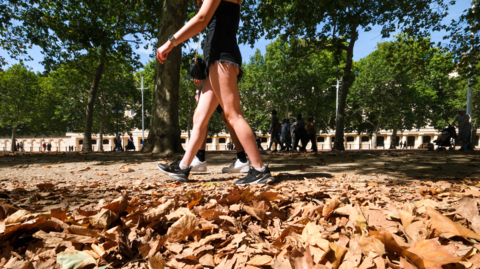 A woman in shorts and trainers walks through fallen leaves amid a UK heatwave