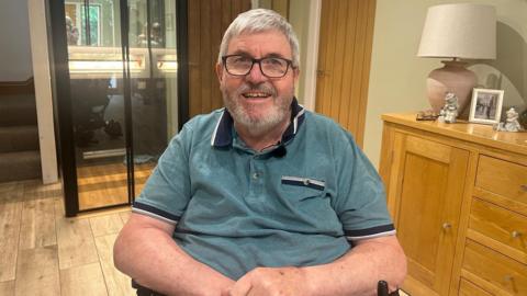 A man in a wheelchair wearing a green polo shirt and glasses