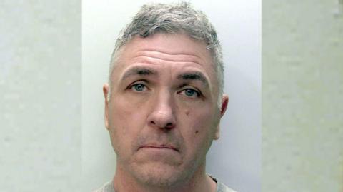 Close up of Paul Butler. Butler is looking into the camera. He is standing against a grey wall.
