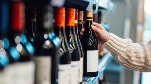 Female hand picking up a bottle of red wine from the shelf in a supermarket.