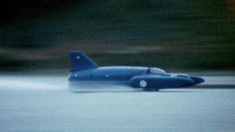 A close-up of Bluebird - a craft that looks like a cross between a plane and a boat. It is painted blue and is running at speed on Coniston Water. It appears to just skim the surface of the water.