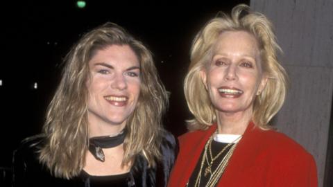 Claire Kellerman pictured with her mum actress Sally Kellerman in 1997. Claire has long, fair hair and wears a dark top and neck scarf. Sally has shoulder-length blonde hair and wears a black top, several gold necklaces and a red blazer. Both smile for the camera.
