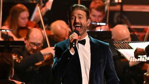 A male singer belting a note at the BBC Proms