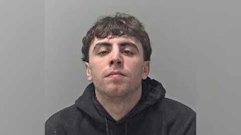 A mugshot of Simon Jones. He is wearing a black hooded top and looking directly into the camera.