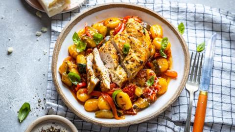 A white plate on a white and blue checked tea towel filled with soft cooked tomatoes and sliced chicken breast