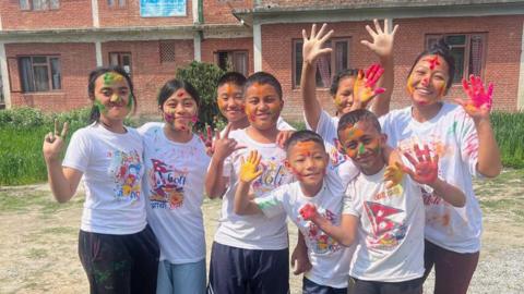 Eight children in white t-shirts with brightly coloured Holi paint on their hands and faces