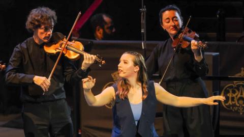 Rhiannon May on stage at the Royal Albert Hall, surrounded by the Aurora Orchestra.