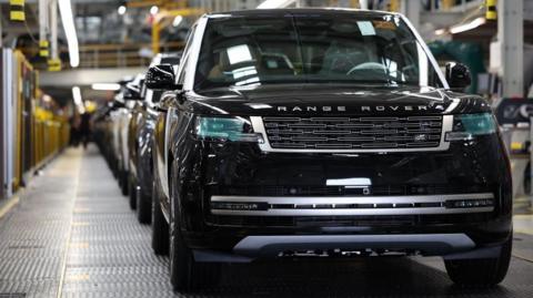 Shiny new cars stand in a line on a spotless factory floor. 