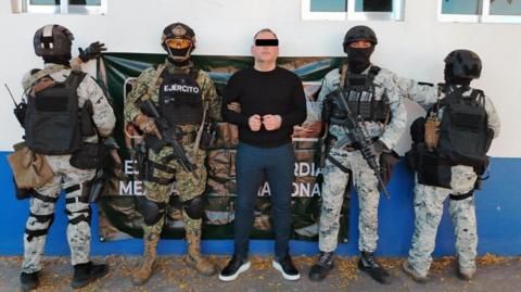 A photo uploaded to social media by Mexico's security minister shows José Ángel Canobbio wearing handcuffs and flanked by armed Mexican soldiers. 