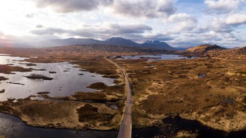 An aerial view of a road crossing Rannoch Moor. The moor is a vast expanse of peat moorland and lochs