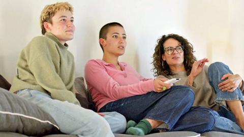 Three people sitting on a sofa watching television