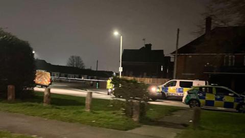 Stanway Road in Gloucester. There are two police vehicles parked up and a couple of officers wearing high vis jackets. Houses can be seen along the road. 