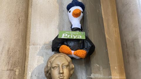 A knitted goose sitting atop a statue of a woman