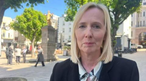 Deputy Catherine Curtis is pictured in the Royal Square. She is wearing a black blazer and has blonde hair.