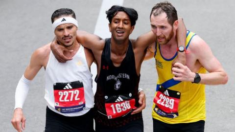 Three runners with their arms around each other crossing a finish line.