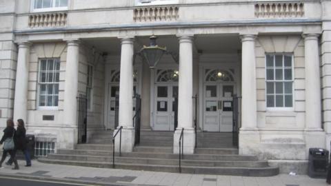 A court building. The court building is made of white brick and has pillars in front of three white doors.