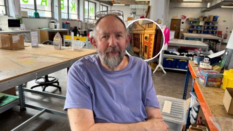 Steve Manners sits inside Hull's Makerspace alongside one of his miniature historical building models, which recreate landmarks from the city's past.