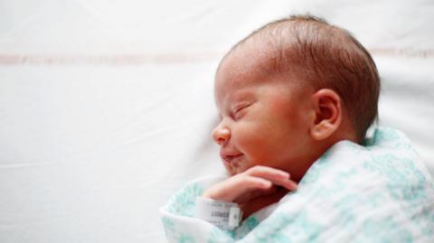 New born baby wrapped in blue and white blanket wearing a name tag on their wrist. 