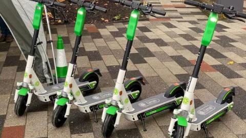 Four e-scooters stood up-right on the pavement