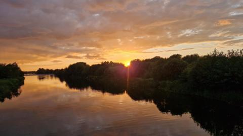 WEDNESDAY - The sunsets over the river with trees on the bank as the river and sky glow orange