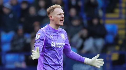 Cameron Dawson, playing in a purple shirt of Rotherham, shouts at his defence