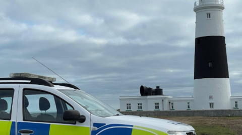 Image of police car parked next to the Alderney lighthouse.