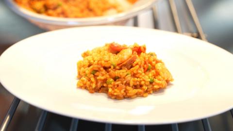 Close up shot of a prawn and chorizo paella dish in the centre of a large white plate. 