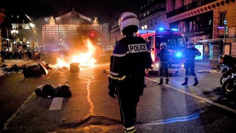 A policeman stands next to a burning pile of rubbish in front of Opera Garnier in Paris