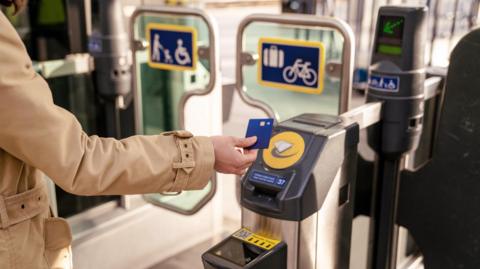 Woman tapping a card to pay to get through a ticket barrier