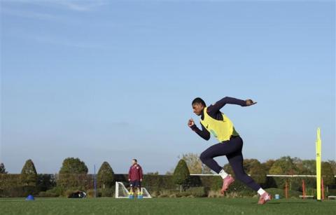 A man, Marcus Rashford, wears a black tracksuit with a yellow high vis vest and football boots. He is running.