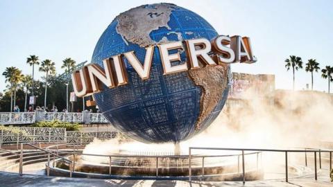 Globe with the word Universal written across it. It is sat on a fountain and misty water is coming upwards around the blue and brown globe. 