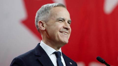 Mark Carney smiles in front of a Canadian flag