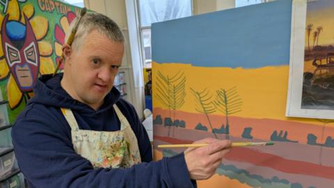 A man standing painting, with a brush in one hand.