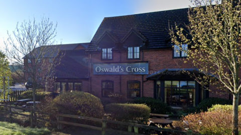 The front of a brown brick building with the words Oswald's Cross on a green sign in gold lettering