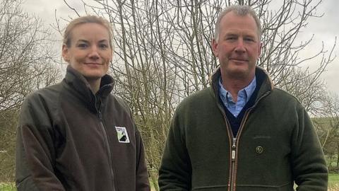 Alice Eley from the Wiltshire Wildlife Trust and farmer Josh Stratton look at the camera while standing in front of the river
