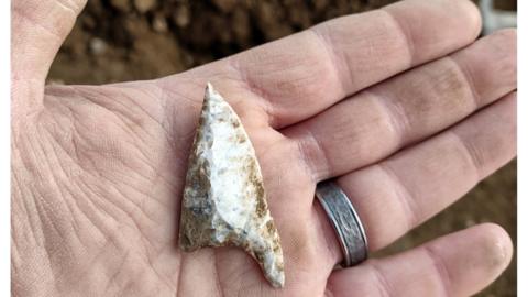 British oblique arrow head in man's hand with wedding ring