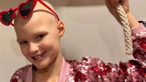 A young girl in a pink top rings a bell.
