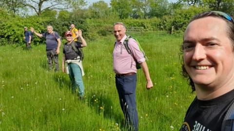 Six people stand in a line searching through long grass.