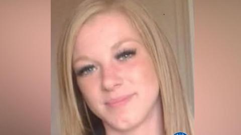 A woman's selfie. She has straight blonde hair to her shoulders and is smiling. She is wearing black false eye lashes.