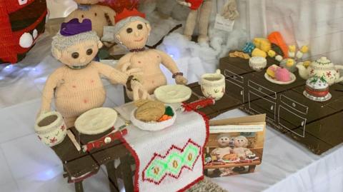 a nude knitted couple at a dinner table with their christmas dinner wearing party hats