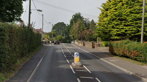 Coombe Street Lane in Yeovil. It is a residential area. A car is driving away from the viewer in the distance.