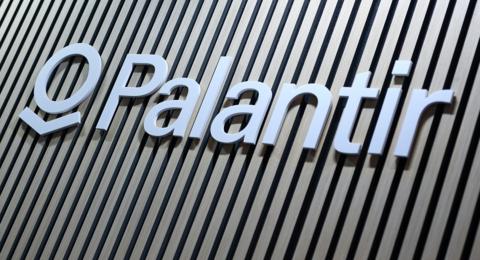 Close-up of the Palantir logo sign in white lettering mounted on a wall with vertical wooden slats in alternating light and dark tones.