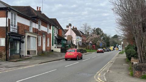 A road with shops, cars and trees along it. 