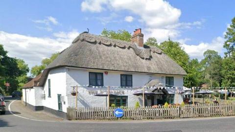 A thatched-roof pub on the corner of a bend in the road.