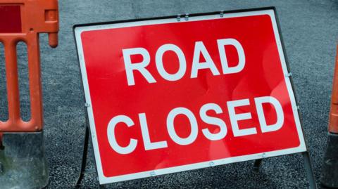 A red sign on a road with white writing reading "ROAD CLOSED" in capital letters.