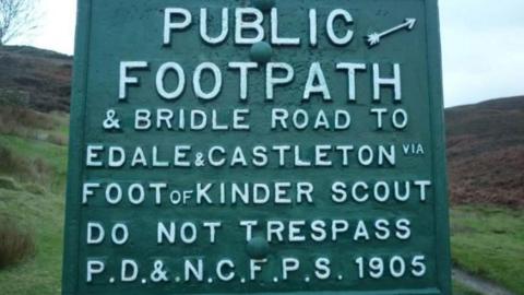 A green sign on a country trail which reads: PUBLIC FOOTPATH AND BRIDAL ROAD TO EDALE AND CASTLETON VIA FOOT OF KINDER SCOUT DO NOT TRESPASS P.D&N.C.F.P.S 1905