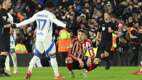 Dan Neil of Sunderland slumps to the ground as Leeds' Largie Ramazani celebrates in front of him