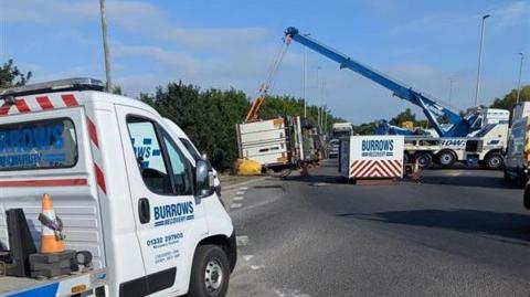 Recovery teams craning the overturned lorry from the side of a roundabout
